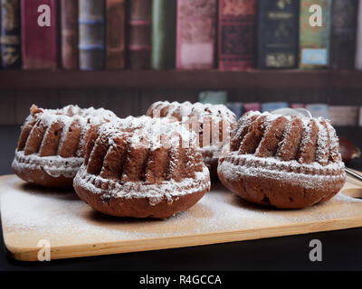 Miniatura Bundt di castagne torte con scaglie di cioccolato su un bambù tagliere, al buio su un sfondo marrone Foto Stock