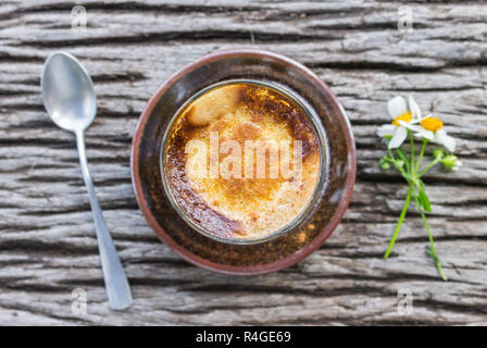 Latte caffè in vetro con fiore a Margherita e il cucchiaio sul tavolo in legno o Flatray tabella superiore Angolo. Caffè classico con fiore in vita naturale concetto. Relax Foto Stock