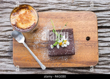 Fiore a margherita sui brownie al cioccolato torta con latte caffè sul tagliere o tagliere in legno Flatray tabella o tabella superiore Angolo. Rilassatevi coffee bre Foto Stock