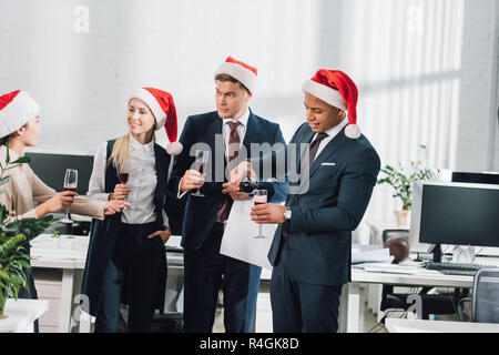 Sorridente multietnica giovani collaboratori a cappelli di Babbo Natale festeggiano il Natale in ufficio Foto Stock