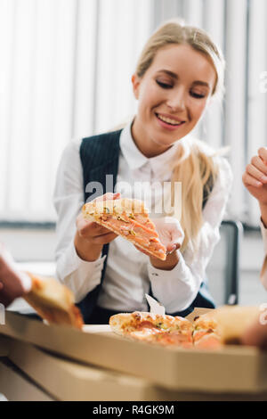 Sorridente giovane imprenditrice di mangiare la pizza con i colleghi in ufficio Foto Stock