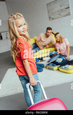 Kid holding valigia mentre la famiglia imballaggio per le vacanze estive sul background, concetto di viaggio Foto Stock