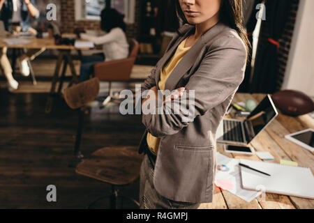 Vista ritagliata della business donna in piedi alla scrivania in ufficio loft con i colleghi su sfondo Foto Stock