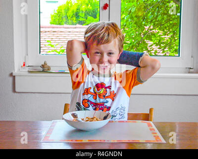 Ragazzo con braccio nel cast ha prima colazione al tavolo Foto Stock