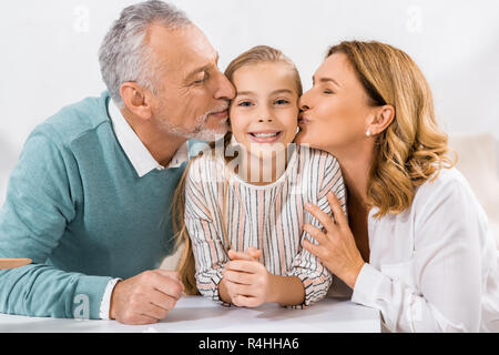 Adorabile bambino guardando la fotocamera mentre i nonni la bacia nelle guance Foto Stock