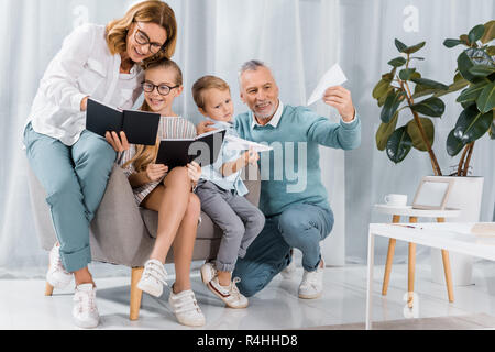 Nonni e nipoti la lettura di libri di testo e giocando con piani di carta sul divano di casa Foto Stock