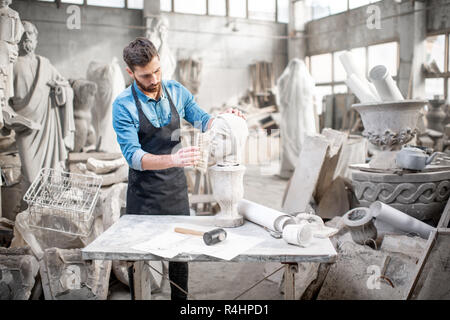 Bello scultore spazzolatura testa in pietra scultura sul tavolo in atmosferica di studio Foto Stock