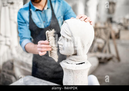 Scultore lavora con la scultura della testa femmina di pulizia con spazzola nel vecchio studio. Vista ravvicinata con nessun volto Foto Stock