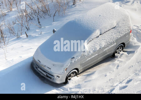 Coperte di neve bianca permanente auto nel parcheggio dopo tempeste. Vista superiore della automobile sulla giornata di sole dopo il cattivo tempo. Concetto di guida in wintertim Foto Stock