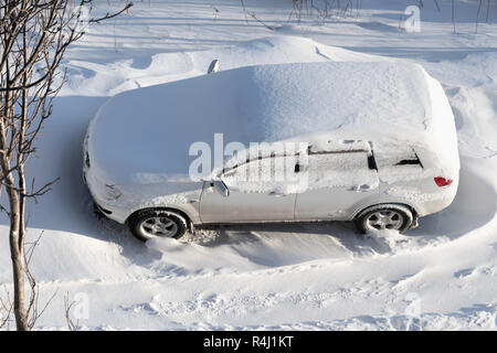 Vista superiore del bianco automobile parcheggiata nel cumulo di neve e rivestita con lo strato di neve dopo la nevicata. Concetto di guida in inverno con la neve sulla strada a poppa Foto Stock