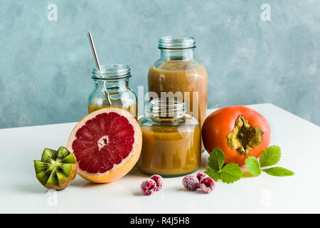 Diversi tipi di bicchieri con freschi Pompelmi, kiwi, persimmon e lampone frullati. sul tavolo bianco e lo sfondo blu. cibo sano. mattina bre Foto Stock