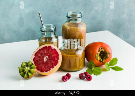 Diversi tipi di bicchieri con freschi Pompelmi, kiwi, persimmon e lampone frullati. sul tavolo bianco e lo sfondo blu. cibo sano. mattina bre Foto Stock