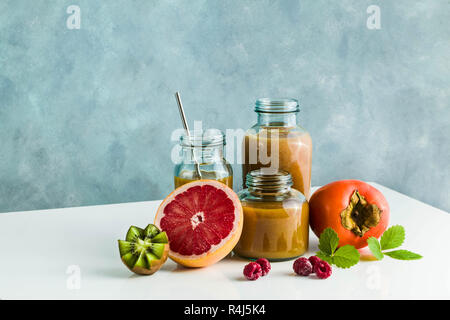 Diversi tipi di bicchieri con freschi Pompelmi, kiwi, persimmon e lampone frullati. sul tavolo bianco e lo sfondo blu. cibo sano. mattina bre Foto Stock