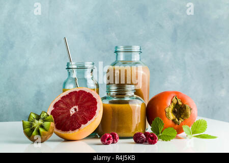 Diversi tipi di bicchieri con freschi Pompelmi, kiwi, persimmon e lampone frullati. sul tavolo bianco e lo sfondo blu. cibo sano. mattina bre Foto Stock