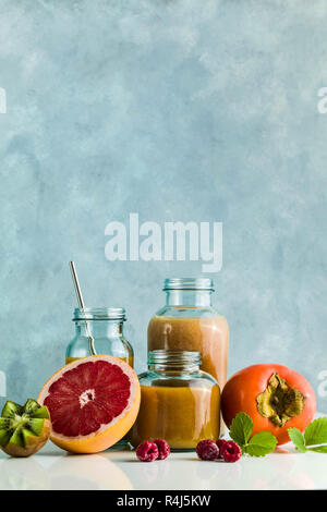 Diversi tipi di bicchieri con freschi Pompelmi, kiwi, persimmon e lampone frullati. sul tavolo bianco e lo sfondo blu. cibo sano. mattina bre Foto Stock