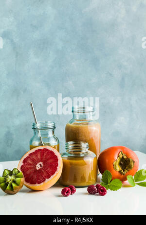 Diversi tipi di bicchieri con freschi Pompelmi, kiwi, persimmon e lampone frullati. sul tavolo bianco e lo sfondo blu. cibo sano. mattina bre Foto Stock