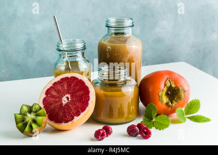 Diversi tipi di bicchieri con freschi Pompelmi, kiwi, persimmon e lampone frullati. sul tavolo bianco e lo sfondo blu. cibo sano. mattina bre Foto Stock