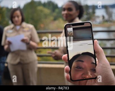 Una madre-figlia in streaming live momento... Come STATI UNITI Air Force Airman 1. Classe Kourtnee Jones si affaccia su , la sua madre, U.S. Navy Chief specialista personale Stacy Gleason, avvolge il suo reenlistment all'Ospedale Navale di Bremerton (NHB), come presiedere reenlistment officer, Lt. La Cmdr. Genaia Hill, NHB Igiene Industriale capo reparto, condivide una nota di congratulazioni da Jones, assegnato alla base comune San Antonio - Fort Sam Houston. Che lo rende un vero affare di famiglia nonostante separati da quasi 1.800 miglia, Master-at-Arms 1a classe Robert Gleason mans il personale della fotocamera del telefono per condividere l'occasione Foto Stock