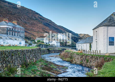 Meandri del fiume che scorre veloce attraverso il piccolo villaggio di Boscastle, Cornwall andando per mare. La mattina presto la luce del sole il rendering di un bel cielo blu. Foto Stock