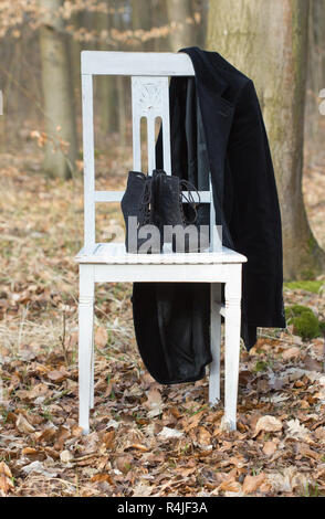 Una sedia bianca con nero scarpe a tacco e giacca nella foresta Foto Stock
