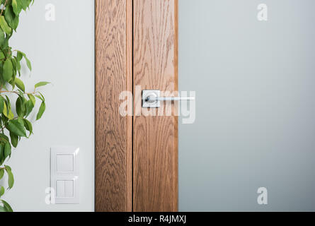 Close-up di elementi interni. Sportello in acciaio manico in legno scuro. Interruttori di bianco sulla parete Foto Stock