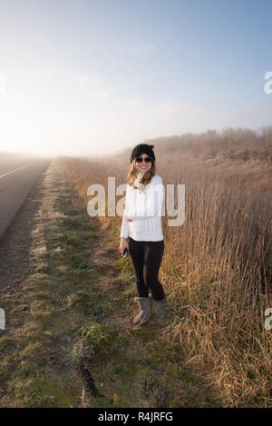 Giovane donna in piedi su un vuoto e strada di nebbia al mattino presto Foto Stock