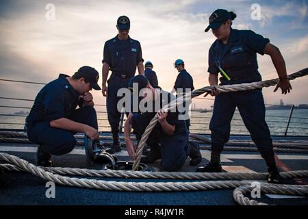 Golfo Arabico (ott. 31, 2018) marinai di alimentazione di una linea di ormeggio verso il basso una griglia dal castello di prua delle visite-missile destroyer USS Jason Dunham (DDG 109) come la nave si diparte, Manama Bahrain a seguito di una programmata visita porta. Jason Dunham è distribuito negli Stati Uniti Quinta Flotta area di operazioni a sostegno di operazioni navali per garantire stabilità marittimo e la sicurezza nella regione centrale di collegamento del Mediterraneo e del Pacifico attraverso l'Oceano Indiano occidentale e tre strategici punti di strozzatura. Foto Stock