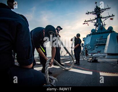 Golfo Arabico (ott. 31, 2018) marinai di alimentazione di una linea di ormeggio verso il basso una griglia dal castello di prua delle visite-missile destroyer USS Jason Dunham (DDG 109) come la nave si diparte, Manama Bahrain a seguito di una programmata visita porta. Jason Dunham è distribuito negli Stati Uniti Quinta Flotta area di operazioni a sostegno di operazioni navali per garantire stabilità marittimo e la sicurezza nella regione centrale di collegamento del Mediterraneo e del Pacifico attraverso l'Oceano Indiano occidentale e tre strategici punti di strozzatura. Foto Stock