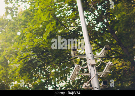 Cluster di telecamere di sicurezza su un lampione in un vecchio parco pubblico sullo sfondo del fogliame a molla Foto Stock