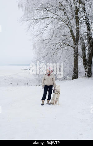 Donna che cammina con un cane in inverno Foto Stock