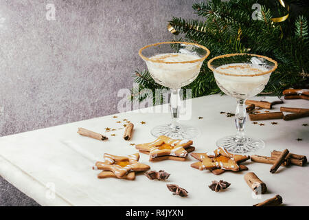 Zabaione latte di Natale cocktail serviti in due vintage bicchieri di cristallo con biscotti di forma a stella i cookie di zucchero, bastoncini di cannella, ramo di abete su bianco Foto Stock