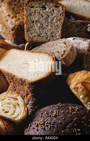 Varietà di freschi di forno segale, scritto, frumento craft pane artigianale, intere e tagliate a fette, nero su sfondo di texture. Close up Foto Stock