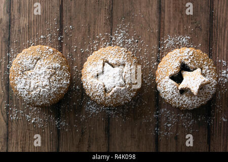 Tre gingerbread frutta crostate di tritare spolverato con zucchero a velo su un sfondo di legno. Foto Stock