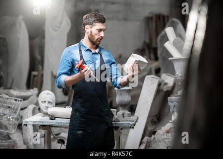 Ritratto di un bel scultore in blu t-shirt grembiule e tenendo vecchio vaso in studio Foto Stock