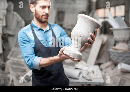 Ritratto di un bel scultore in blu t-shirt grembiule e tenendo vecchio vaso in studio Foto Stock