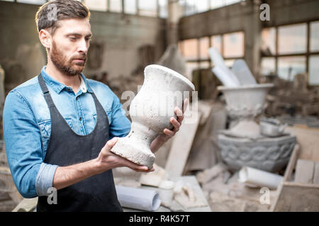 Ritratto di un bel scultore in blu t-shirt grembiule e tenendo vecchio vaso in studio Foto Stock