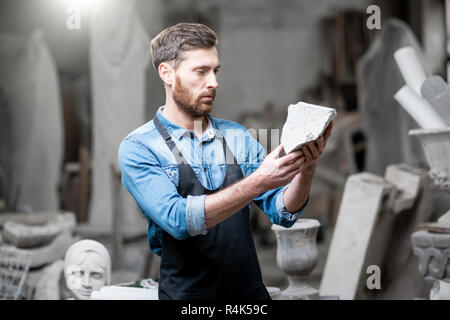 Ritratto di un bel scultore in blu t-shirt grembiule e tenendo in mano un pezzo di pietra in studio Foto Stock