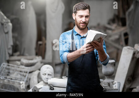 Ritratto di un bel scultore in blu t-shirt grembiule e tenendo in mano un pezzo di pietra in studio Foto Stock