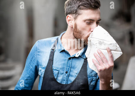 Ritratto di un bel scultore in blu t-shirt grembiule e tenendo in mano un pezzo di pietra in studio Foto Stock