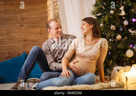 Foto di felice coppia incinta su sfondo dell albero di Natale decorato Foto Stock