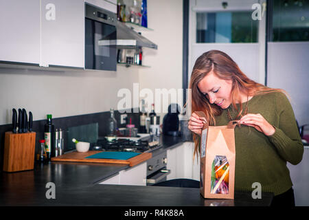 Giovane donna apre un pacchetto di ingredienti freschi per cena salutare Foto Stock