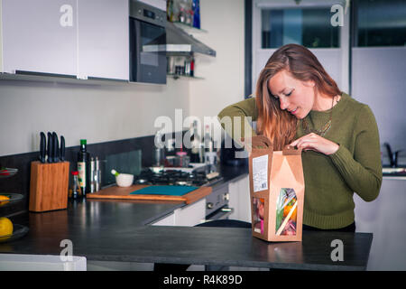 Giovane donna apre un pacchetto di ingredienti freschi per fare una sana cena. Foto Stock