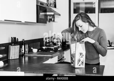 Giovane donna apre un pacchetto di ingredienti freschi per fare una sana cena. Foto Stock