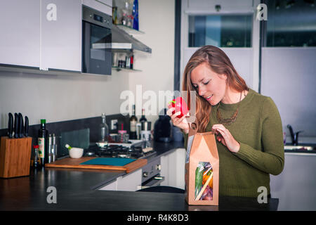 Giovane donna apre un pacchetto di ingredienti freschi per cena salutare e tenendo la paprica Foto Stock