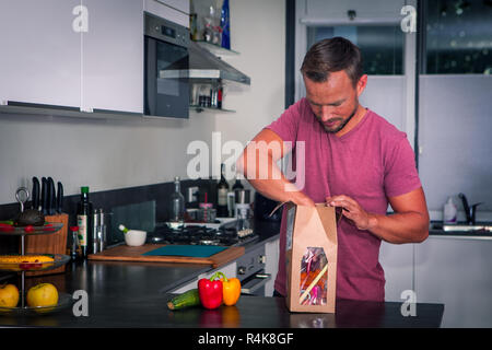 Giovane uomo apre un pacchetto di ingredienti freschi per fare una sana cena Foto Stock