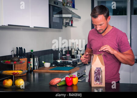 Giovane uomo apre un pacchetto di ingredienti freschi per fare una sana cena Foto Stock