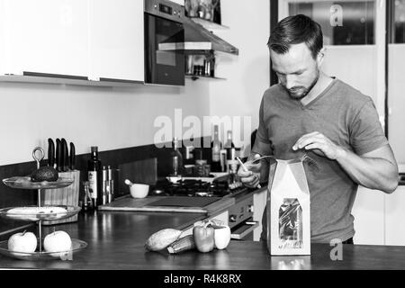 Giovane uomo apre un pacchetto di ingredienti freschi per fare una sana cena Foto Stock