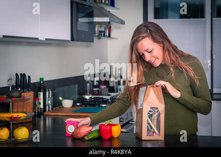 Giovane donna apre un pacchetto di ingredienti freschi per fare una sana cena Foto Stock