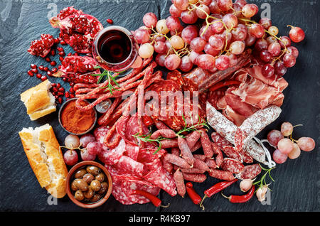 Ampia scelta di tapas. Una pietra tagliere con salumi. Lo spagnolo salumi, jamon, chistorra, chorizo, salchichon, con un bicchiere di vino rosso, olive, gra Foto Stock