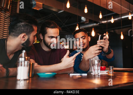 Gruppo di razza mista giovani uomini a parlare e utilizzando il telefono nel lounge bar. Multirazziale amici divertendosi in cafe di bere il caffè Foto Stock